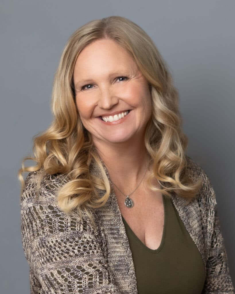 Portrait of Rev. Sherri Cunningham, smiling, with long blonde hair and a knit cardigan