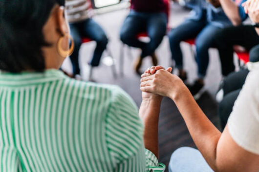 Close-up of people with holding hands in a group therapy